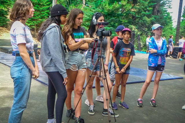 Group of teens learning filmmaking at summer camp in the forest.