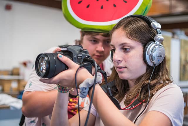 Young campers at photography workshop, one holding a camera and the other wearing headphones at a summer camp. Young campers at photography workshop, one holding a camera and the other wearing headphones at a summer camp.