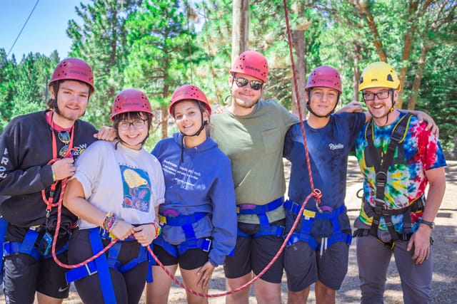 Group of young adults in helmets and harnesses at a summer camp ropes course. Group of young adults in helmets and harnesses at a summer camp ropes course.