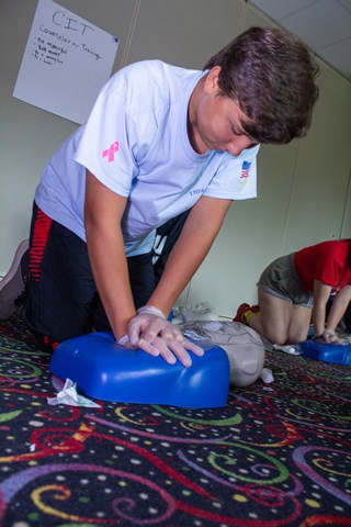 Teen learning CPR at summer camp training session, practicing on a mannequin for emergency readiness skills. Teen learning CPR at summer camp training session, practicing on a mannequin for emergency readiness skills.