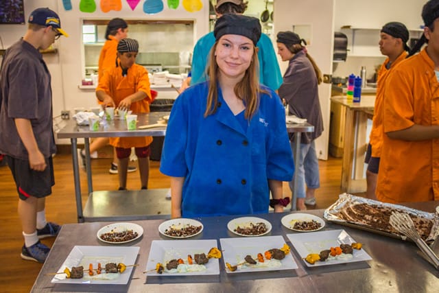 Summer camp cooking class with teens learning culinary skills in a kitchen setting, presenting plated dishes. Summer camp cooking class with teens learning culinary skills in a kitchen setting, presenting plated dishes.
