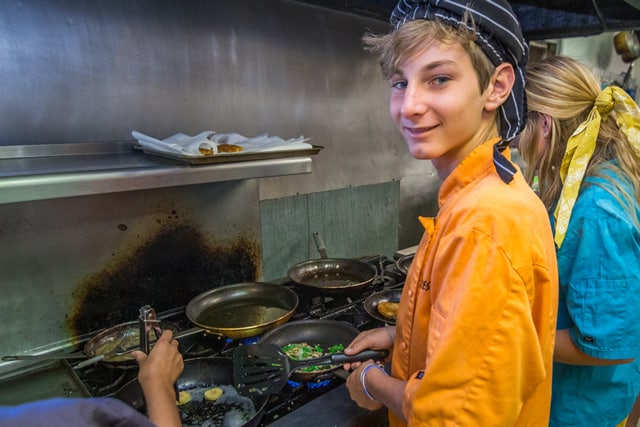 Teen camper cooking in a kitchen at a summer camp, learning culinary skills and teamwork. Teen camper cooking in a kitchen at a summer camp, learning culinary skills and teamwork.