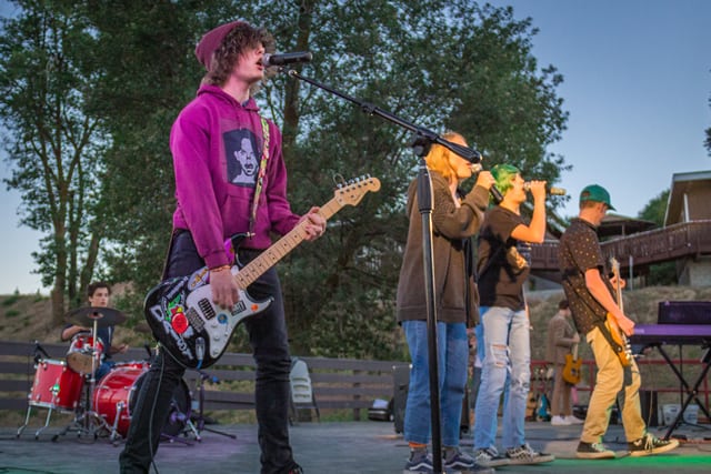 Teens performing in a rock band at a summer camp, playing guitar, drums, and singing outdoors. Teens performing in a rock band at a summer camp, playing guitar, drums, and singing outdoors.
