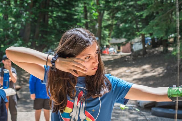 Teen practicing archery at summer camp in forest setting. Skills and fun in outdoor adventure activities.
