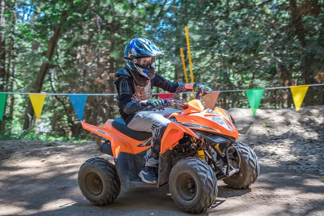 Child enjoying ATV riding at summer camp, surrounded by trees and colorful flags. Perfect adventure for young thrill-seekers! Child enjoying ATV riding at summer camp, surrounded by trees and colorful flags. Perfect adventure for young thrill-seekers!