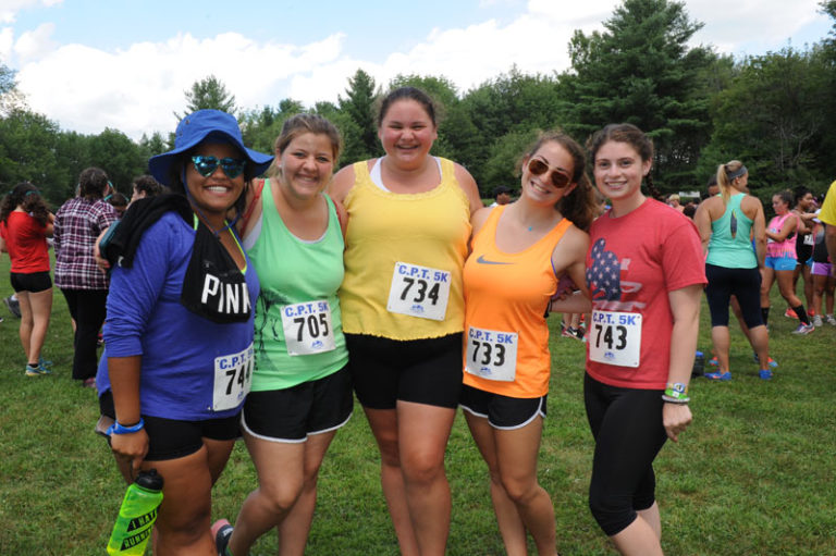 Group of friends posing at a summer camp 5K run event, wearing colorful shirts and race bibs, enjoying the outdoors. Group of friends posing at a summer camp 5K run event, wearing colorful shirts and race bibs, enjoying the outdoors.