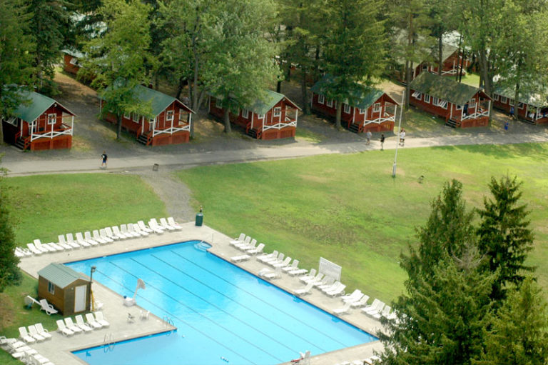 Aerial view of summer camp with cabins and pool, surrounded by trees, ideal for outdoor activities and youth programs. Aerial view of summer camp with cabins and pool, surrounded by trees, ideal for outdoor activities and youth programs.