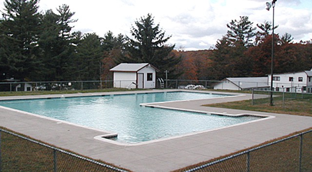 Spacious pool surrounded by trees at a summer camp, perfect for swimming and outdoor activities.
