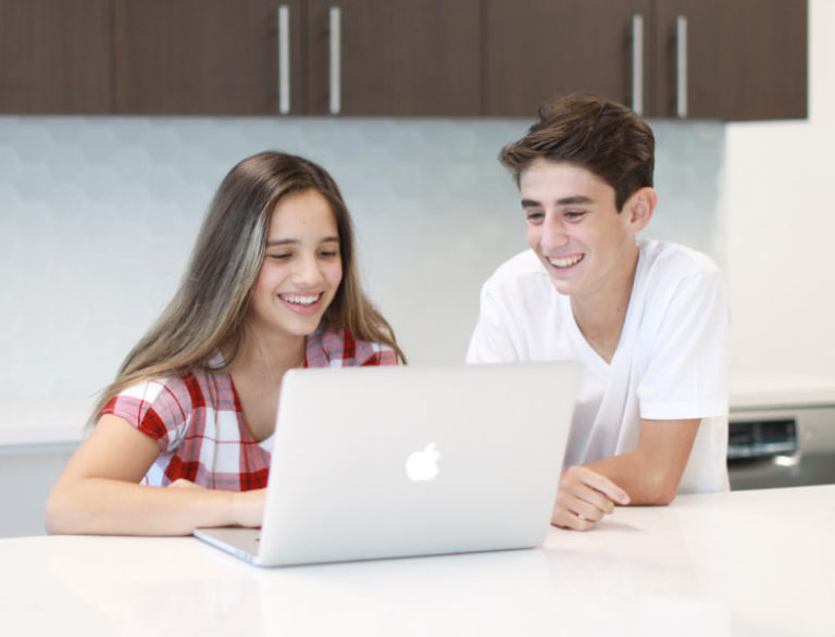 Two kids smiling at a laptop, exploring summer camp options online. Two kids smiling at a laptop, exploring summer camp options online.
