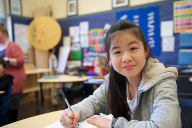 Young girl enjoying activities at summer camp, writing in classroom setting. Perfect for exploring camp programs.