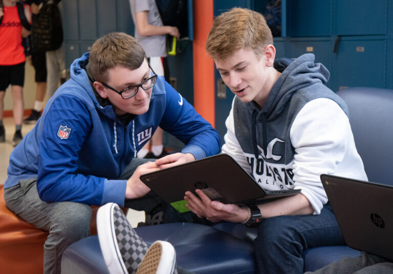 Two teens collaborate over a laptop in a school setting, discussing summer camp activities and programs. Two teens collaborate over a laptop in a school setting, discussing summer camp activities and programs.