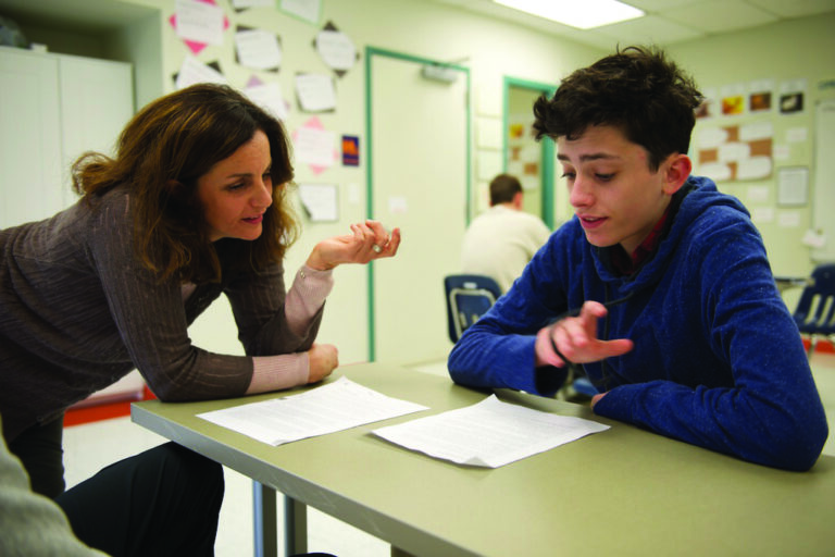 Engaged teacher and student collaborating on summer camp project at a desk with papers in a classroom setting.