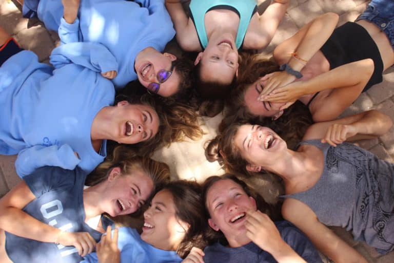 Group of happy girls lying in a circle, laughing at summer camp. Fun and friendship at youth camps.