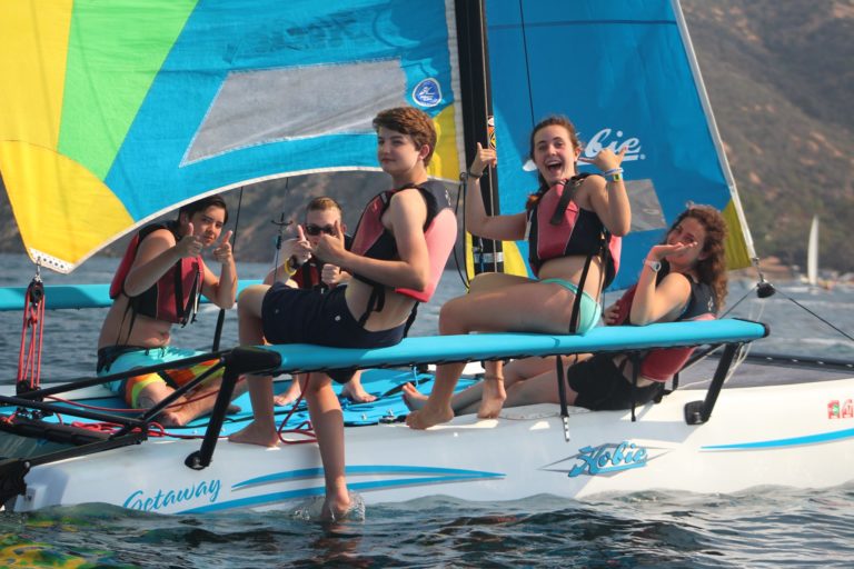 Teens sailing and having fun at summer camp on a catamaran, wearing life jackets. Teens sailing and having fun at summer camp on a catamaran, wearing life jackets.