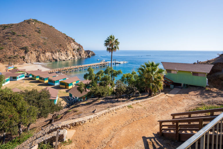 Scenic view of a coastal summer camp with cabins, pier, and ocean backdrop for adventure-filled experiences.