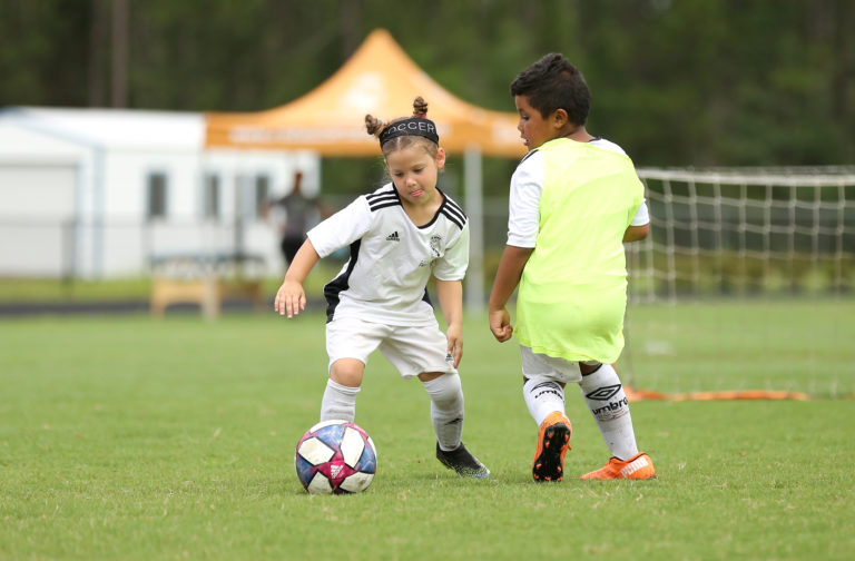 Kids playing soccer at summer camp, focusing on teamwork and skills on the green field. Soccer camp fun.
