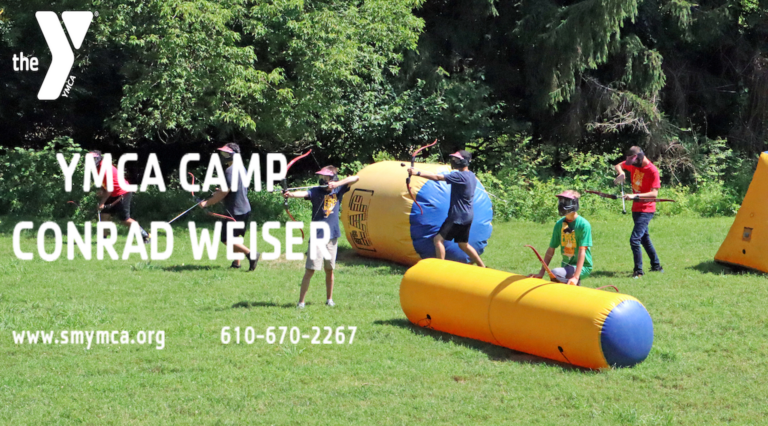 Kids playing archery tag at YMCA Camp Conrad Weiser, surrounded by green trees and inflatable barriers.