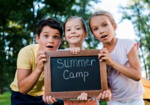 Kids holding a Summer Camp sign at a campsite; perfect for a fun summer adventure.