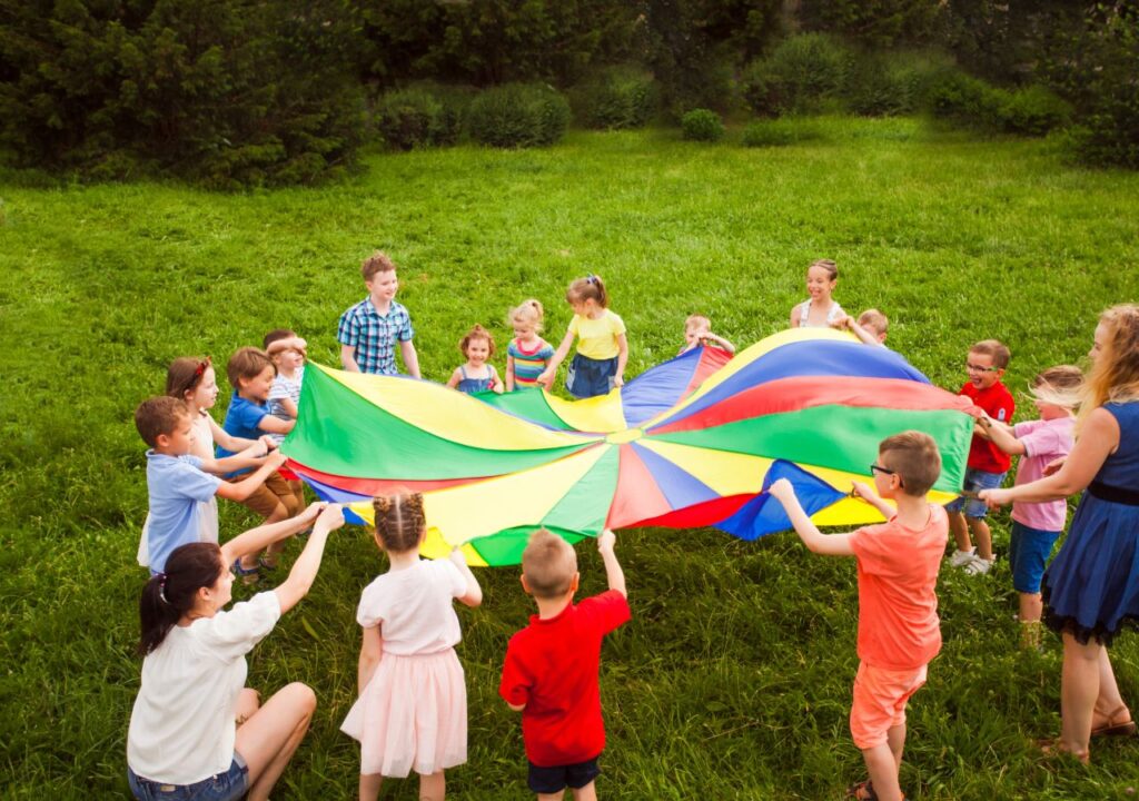Group of kids enjoying parachute games at summer camp in a grassy field.