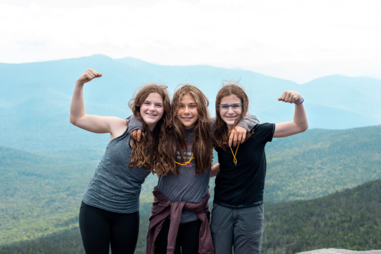 Three girls smiling and flexing at a mountain view during summer camp adventure. Perfect outdoor activity for youth. Three girls smiling and flexing at a mountain view during summer camp adventure. Perfect outdoor activity for youth.