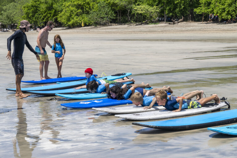 Kids learning to surf on a beach at summer camp with instructors guiding them. Perfect outdoor adventure experience. Kids learning to surf on a beach at summer camp with instructors guiding them. Perfect outdoor adventure experience.
