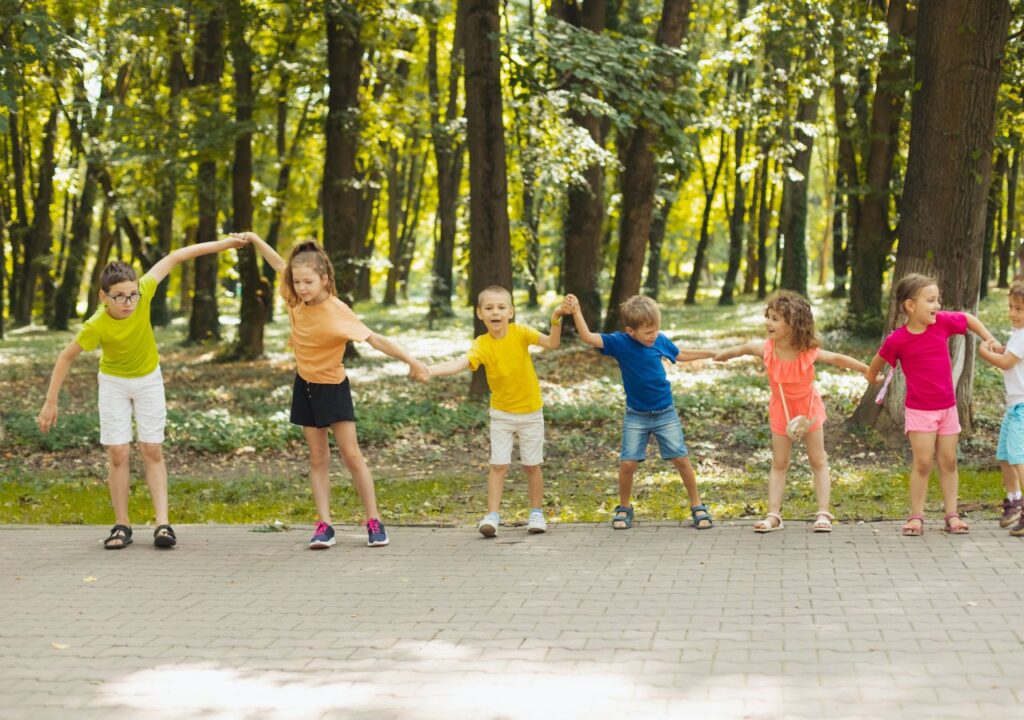 Children playing in a forest at summer camp, holding hands and having fun in the sun.