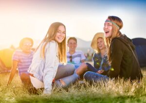 A group of teenagers smiling and sitting on the grass with a background of the mountain.