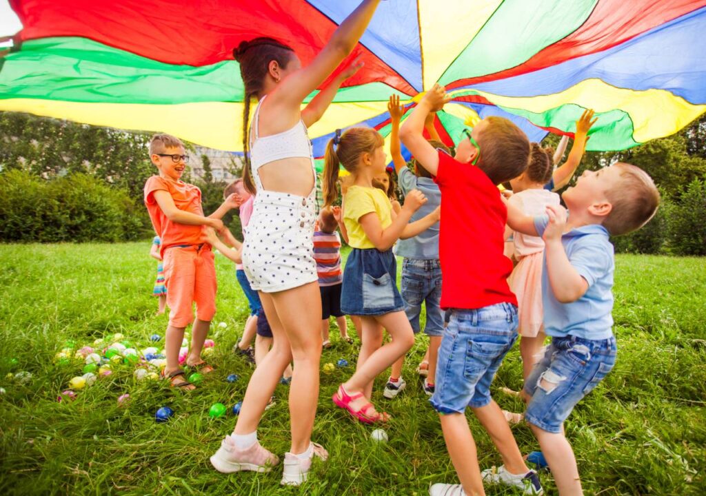 Children playing with a colorful parachute in a park.