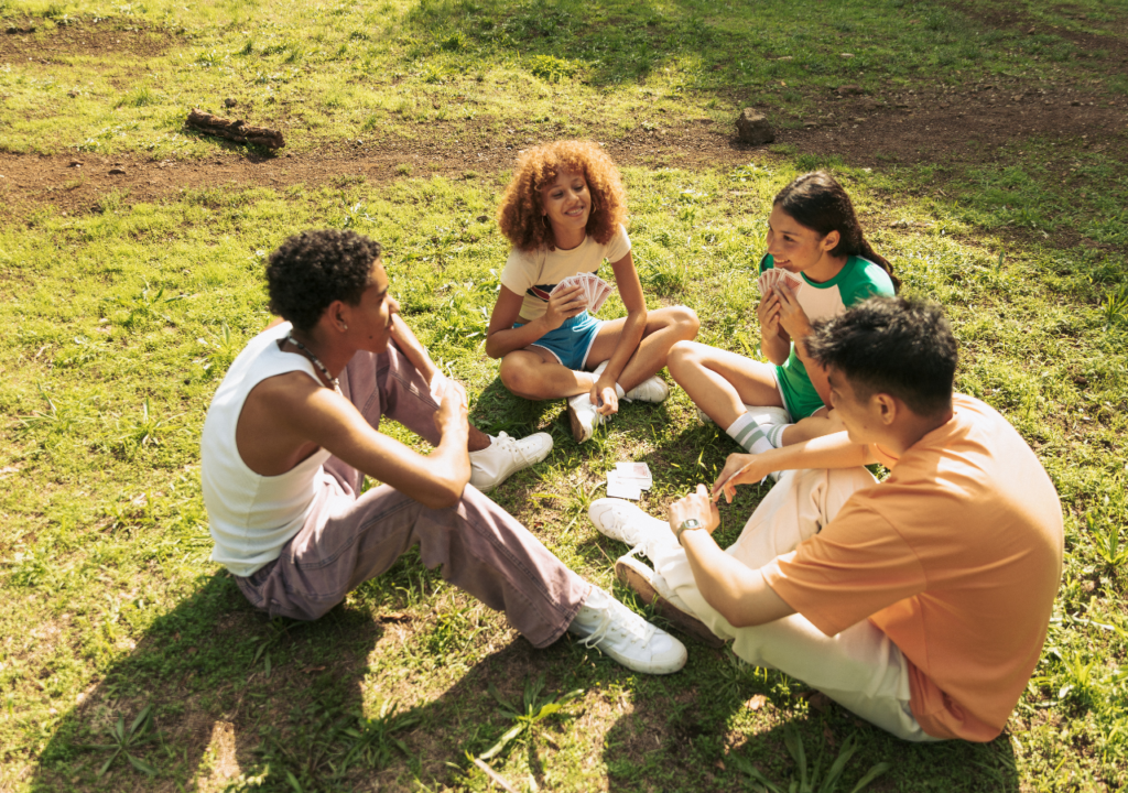Teens playing cards outdoors at a summer camp, bonding in nature, fostering friendships and fun activities.