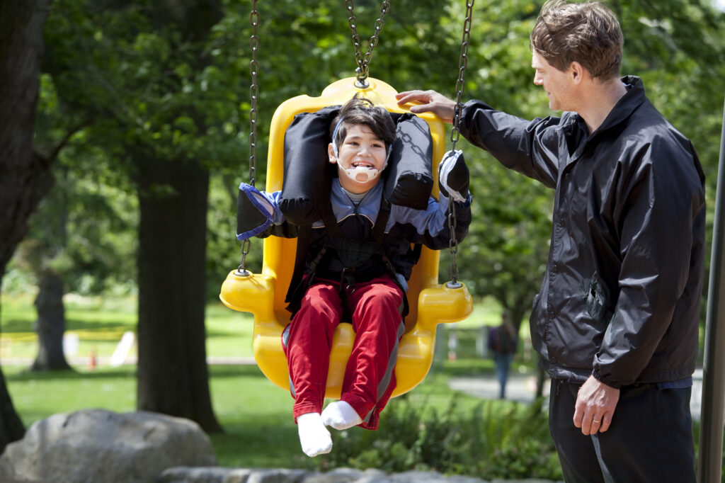 Child enjoying adaptive swing with counselor at summer camp playground.