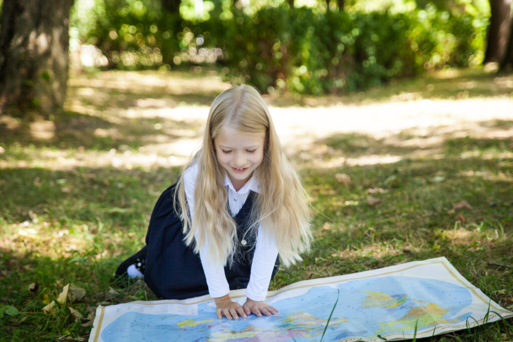 Child exploring a map outdoors at summer camp, learning navigation skills under the trees.