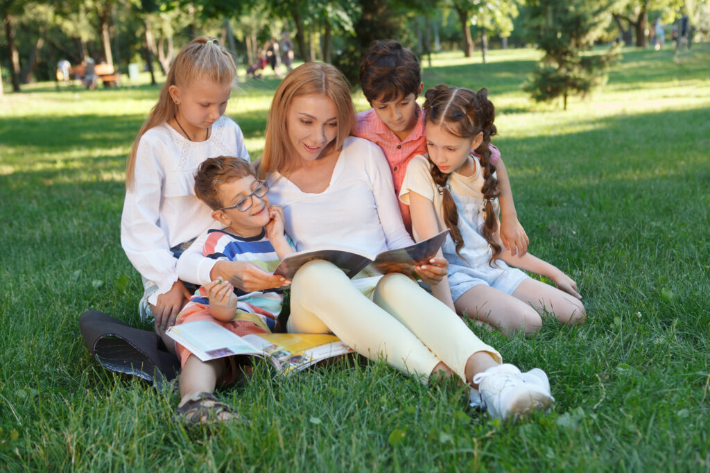 Kids enjoying a storytime session outdoors at summer camp, surrounded by nature and greenery.