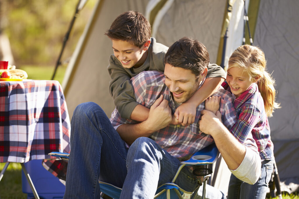 Family enjoying summer camp fun with kids playing and laughing outside tent.