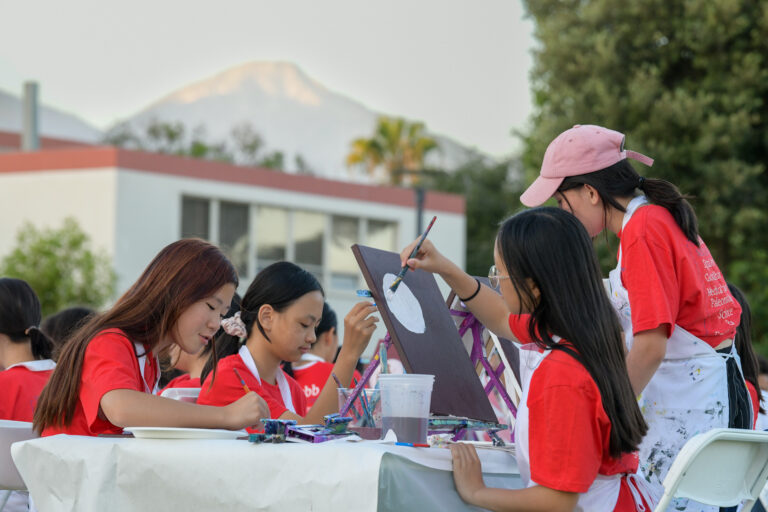 Kids painting outdoors at summer camp, engaging in creative activities with mountains in the background.