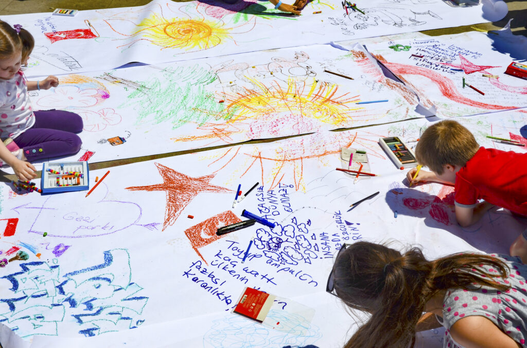 Kids drawing colorful art on large paper at a summer camp activity.