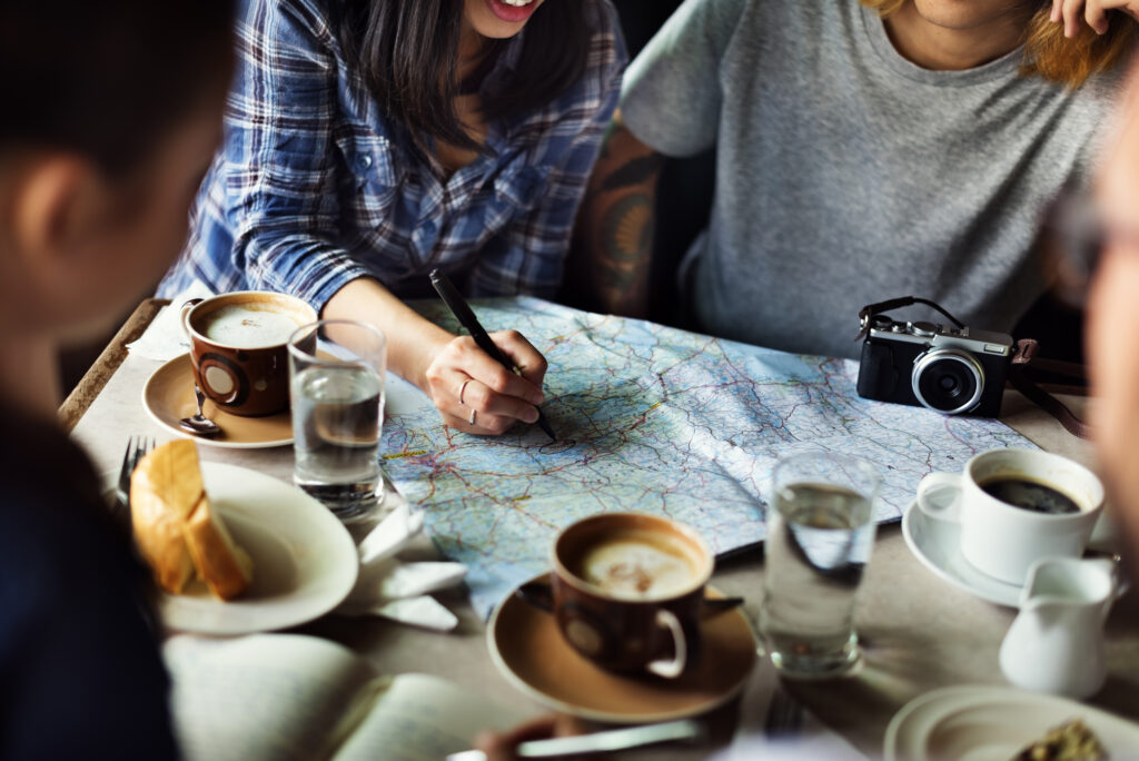 Group planning summer camp trip, marking map at cafe table.