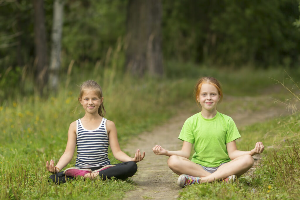 Kids practicing outdoor yoga meditation at summer camp for a nature-focused wellness activity.