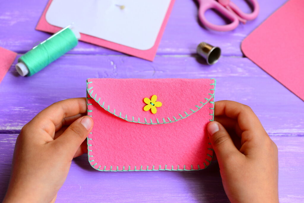 Child's hands holding a handmade pink felt pouch at a crafting summer camp activity.