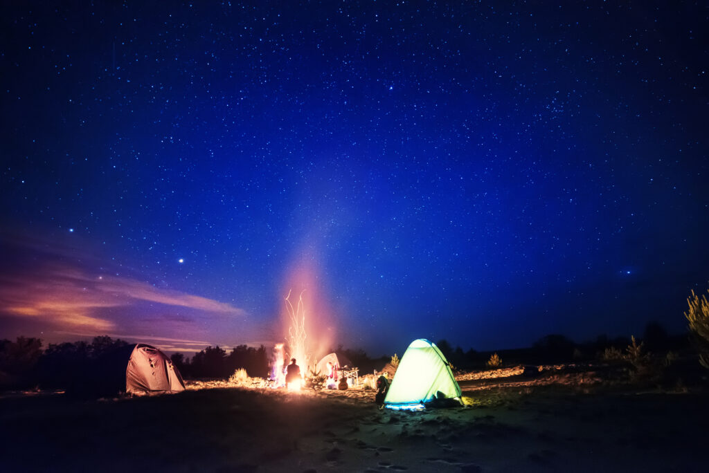 Starry night at summer camp with tents and a campfire, perfect for outdoor adventure under the stars.