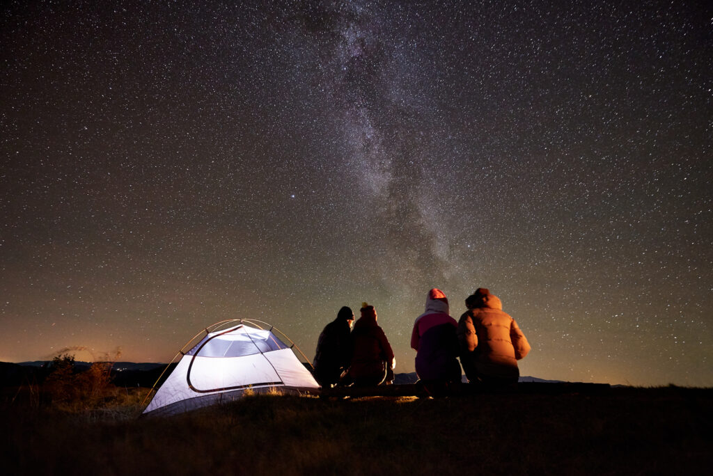Campers stargazing by a tent under a starry sky at summer camp.