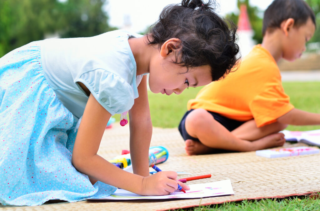 Children drawing at a summer camp, enjoying outdoor creativity and art activities on a sunny day.