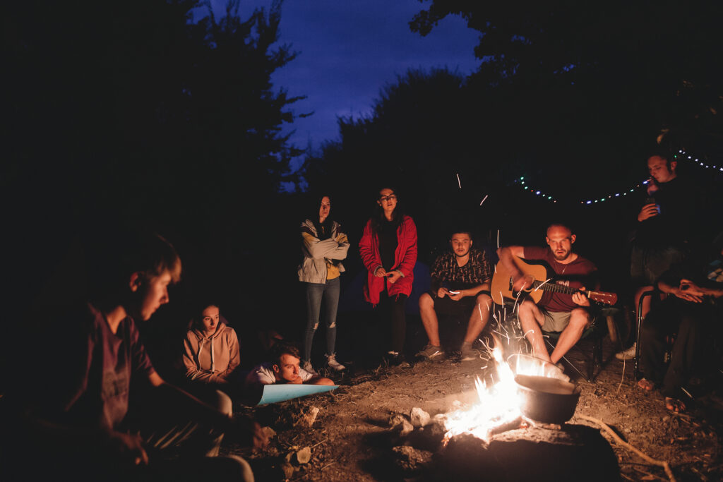 Campers enjoying a cozy night around a campfire with guitar music at summer camp.