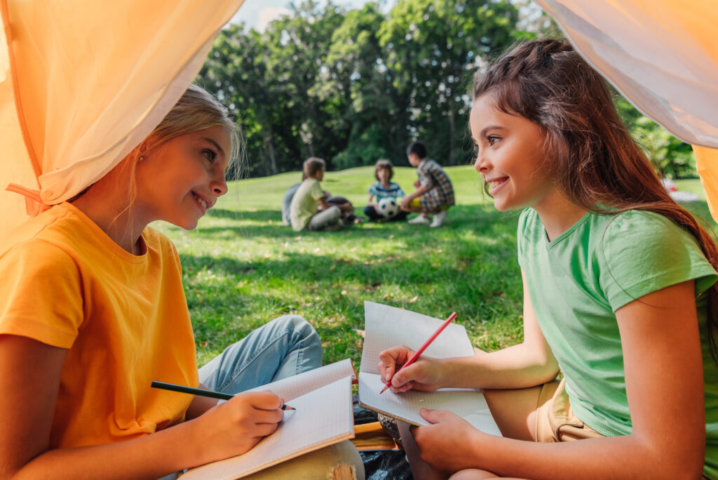 Girls drawing in a summer camp tent, enjoying outdoor activities. Perfect summer camp experience for kids.