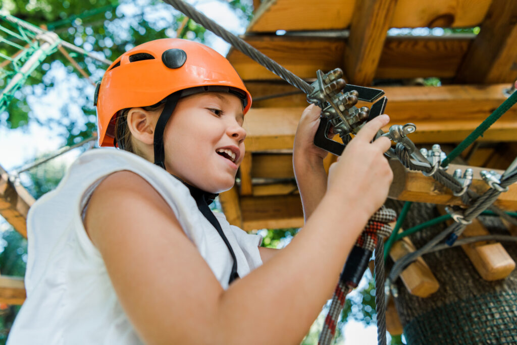 Child enjoying a ropes course at summer camp, wearing an orange helmet for safety and adventure fun.
