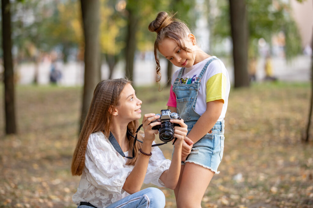 Girl showing camera to young camper outdoors at summer camp