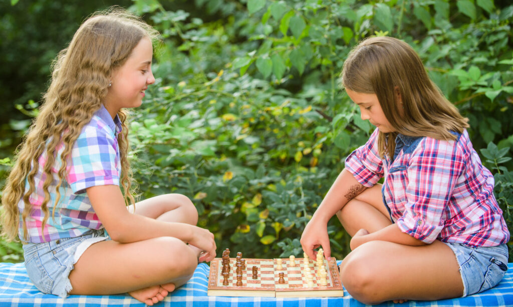 Two girls playing chess outside at summer camp, enhancing strategic thinking and fun in nature.