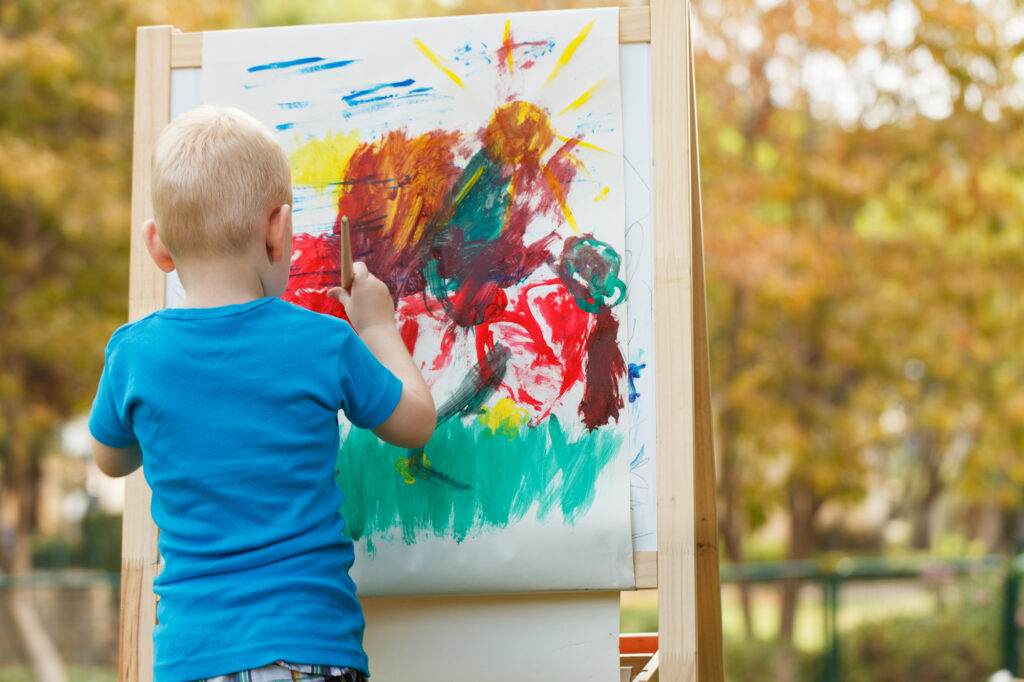 Child painting at summer camp, exploring creativity outdoors with vibrant colors.