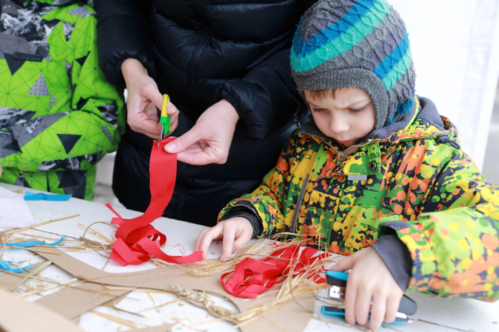 Child crafting with red ribbon at a summer camp art activity.