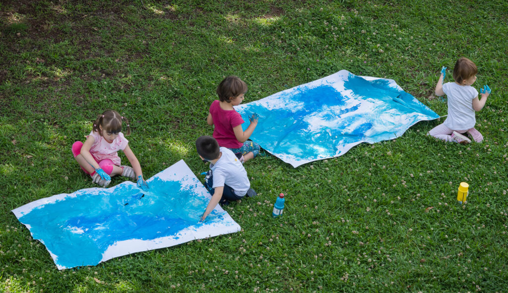 Children enjoying outdoor painting activities at summer camp on a grassy field.