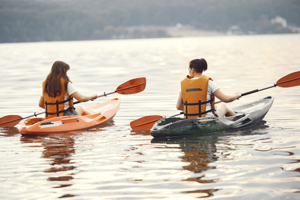 Two campers kayaking on a lake at summer camp, wearing life jackets and enjoying outdoor adventure.